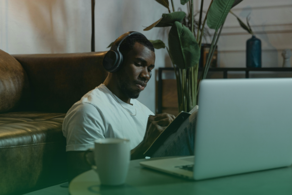Homem lendo com notebook a frente e caneca ao lado do notebook.
